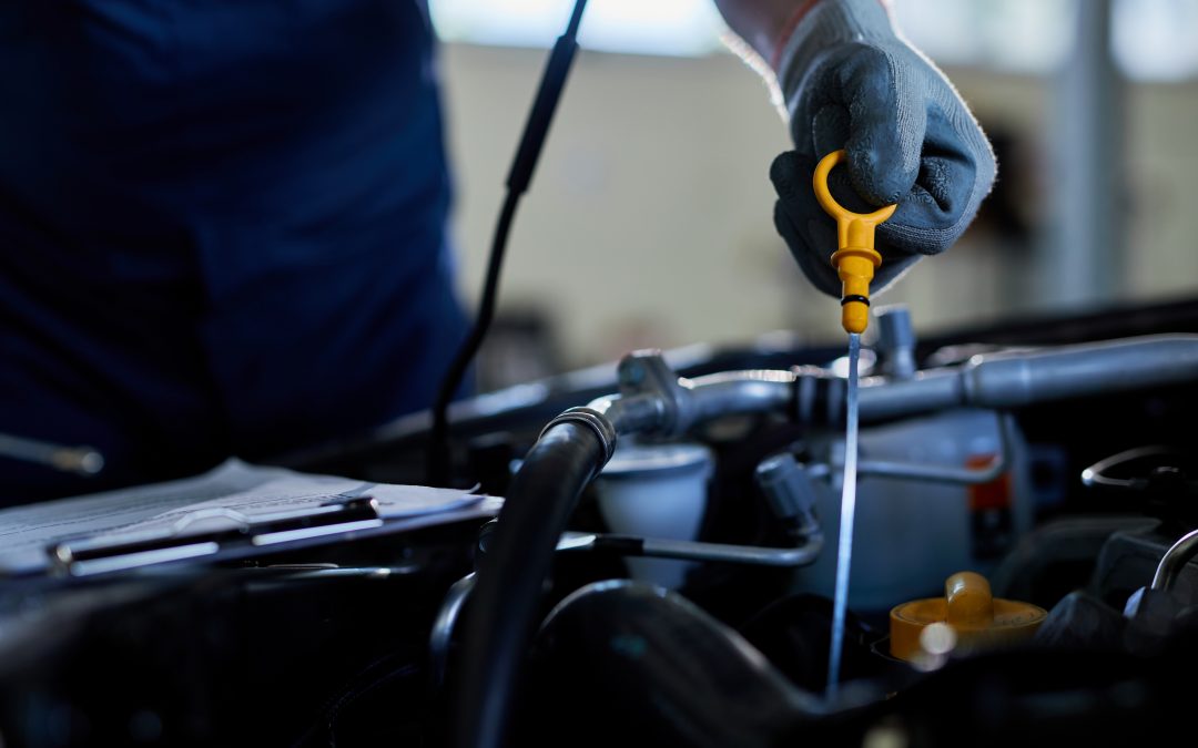 Close-up of a mechanic's hand wearing a glove, checking a car's oil level with a dipstick.