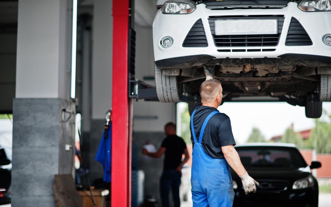 Mechanic in blue overalls inspects a car on a hydraulic lift in the bustling auto repair shop.