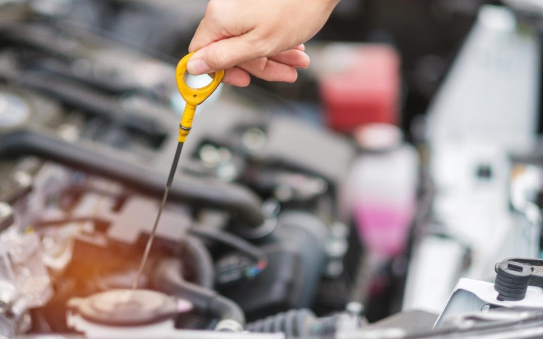 How Often Should You Change Your Oil A hand checking car oil with a dipstick in an open engine bay.