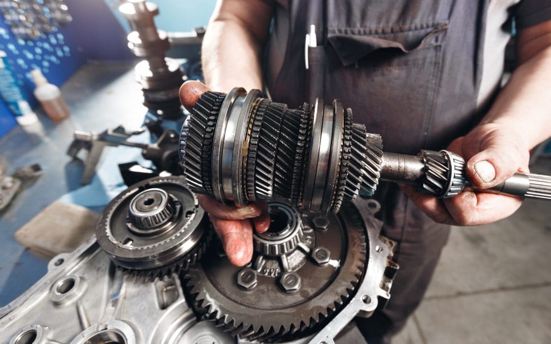 Transmission Issues Mechanic holding a car gearbox component with gears, hands slightly greasy, automotive workshop background.