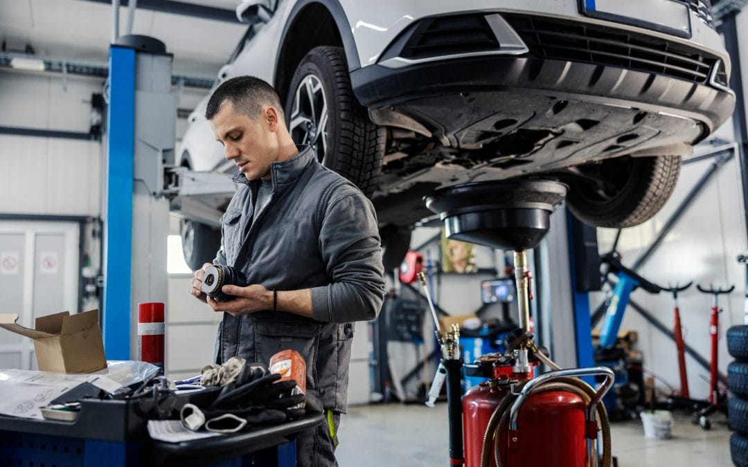 auto repair shop Mechanic at work, inspecting a part in an auto repair shop with a car lifted on a hydraulic lift in the background.