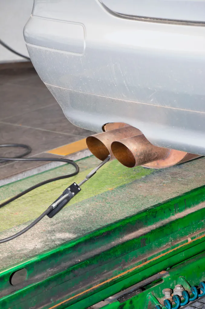A sensor probes a car's exhaust pipes on a dynamometer, measuring emissions during a test.