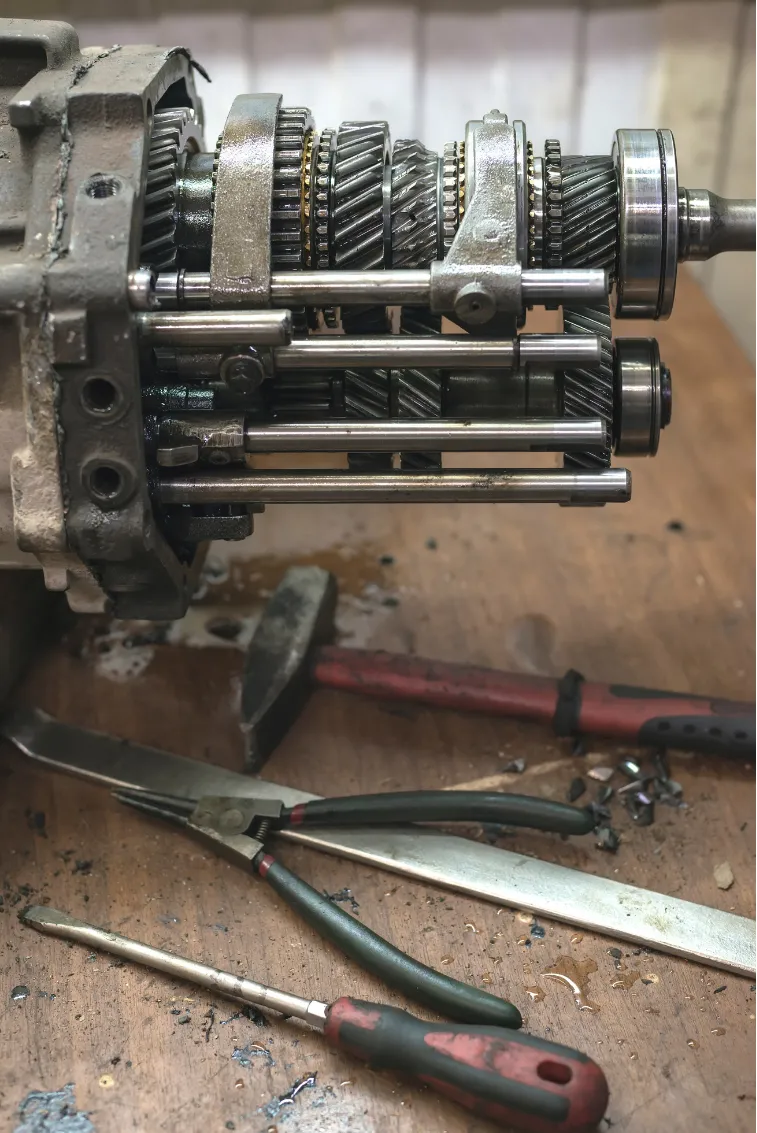 transmission-1 Close-up of a disassembled gearbox on a workbench with various hand tools scattered nearby.