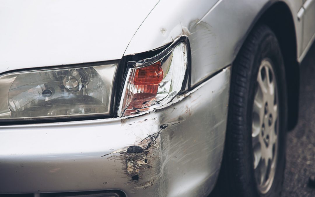 Close-up of a silver car with a damaged front bumper and a broken headlight on the driver's side.