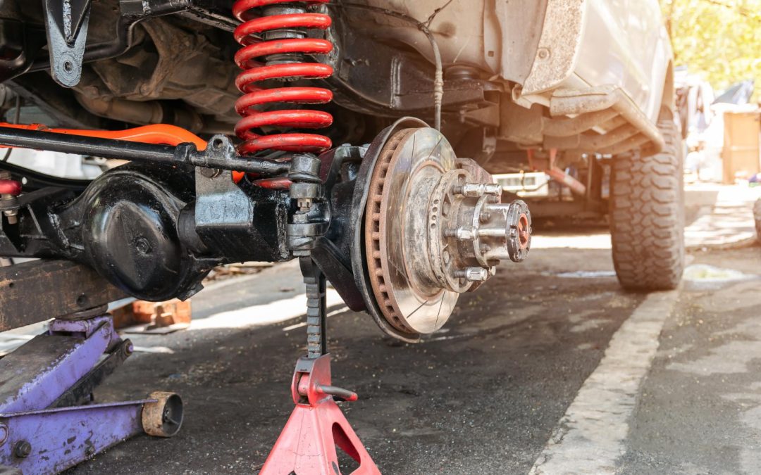 A car on a jack stand with the wheel removed shows the exposed suspension and brake components.