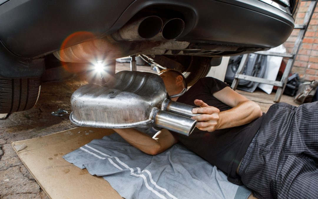 A mechanic lying on the ground installs a car exhaust muffler.